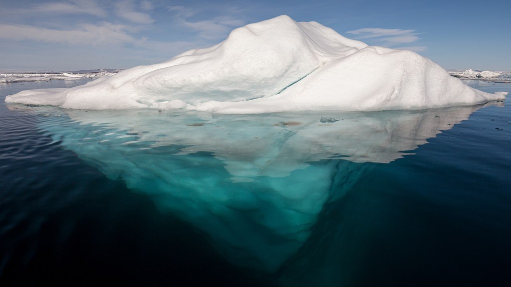 A iceberg floating in the arctic. The ice under the water is much larger than the ice above the water.